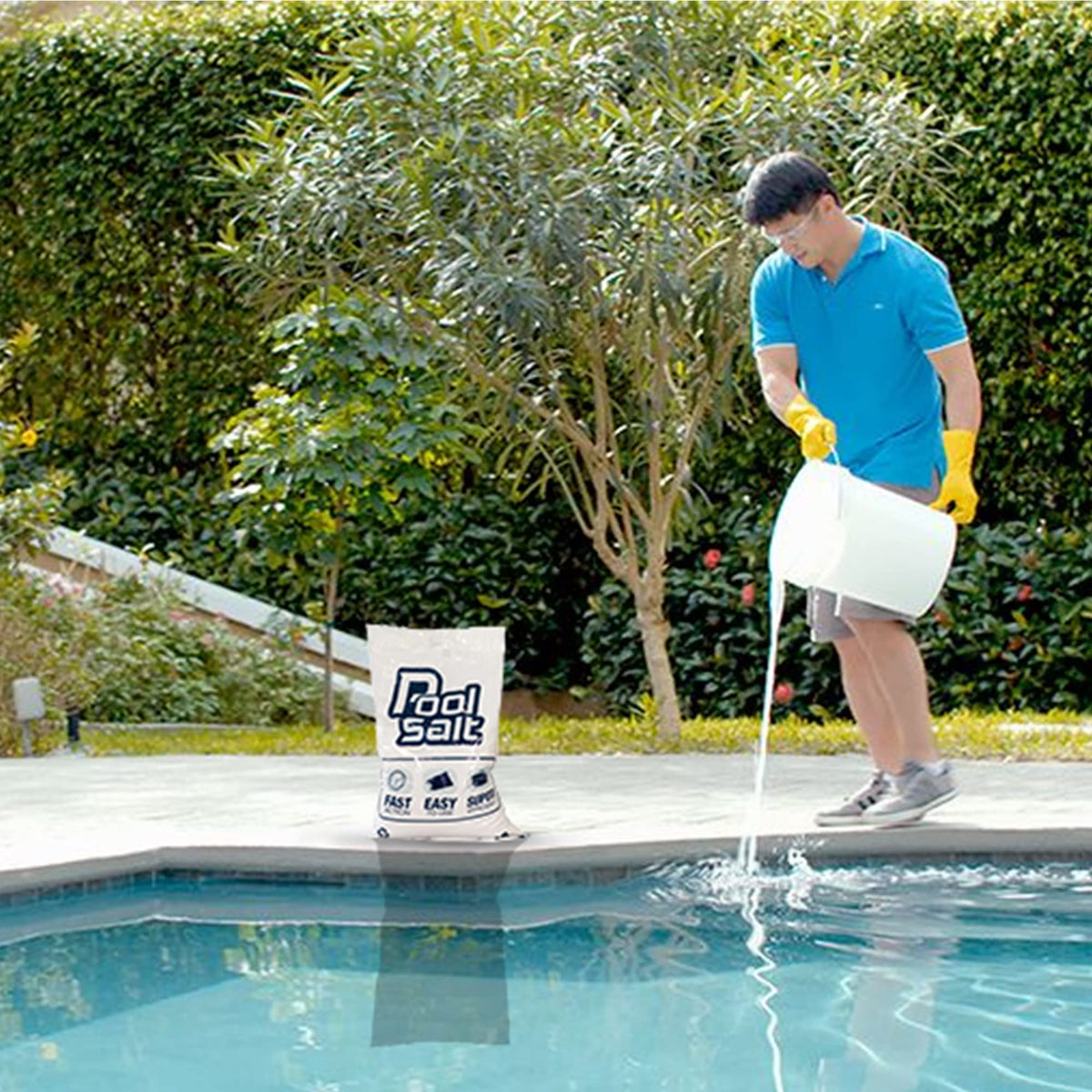 Man pouring dissolved pool salt from a bucket into a pool beside a Pool Salt bag.