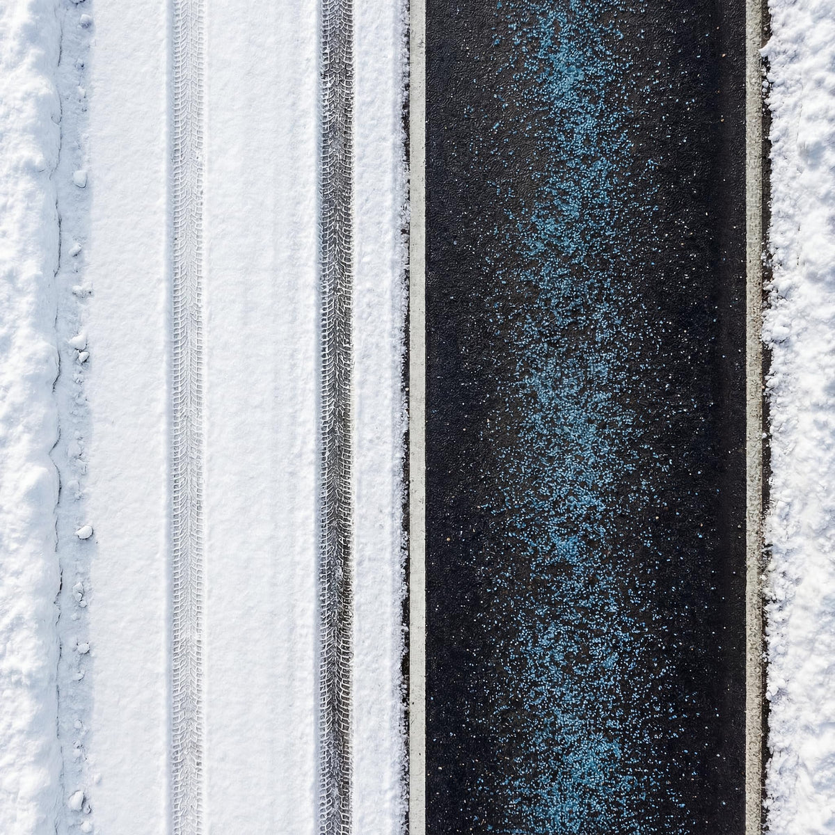 Overhead view of blue ice melt granules spread down a dark driveway between snow.