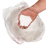 Hand holding white calcium chloride pellets over an open bag.