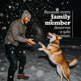 Man playing with a dog in falling snow at night.
