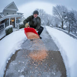 Man spreading orange ice melt from a red scoop on a snowy front walk.