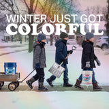Three children carrying a shovel and colored ice melt pails down a snowy sidewalk.