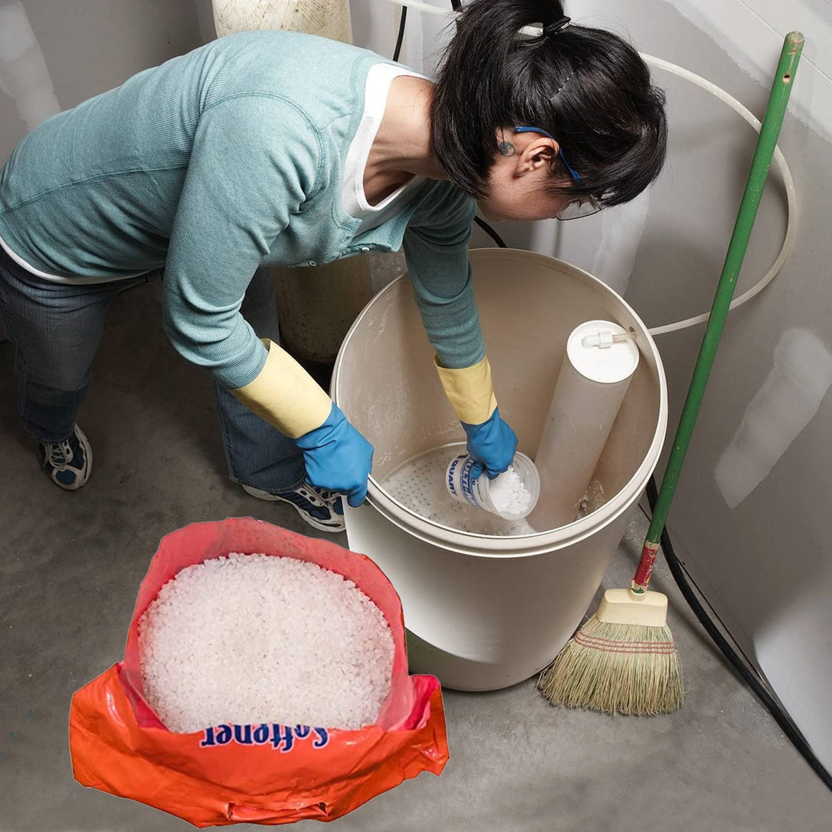 Person filling a water softener brine tank, with an open Softener Shield bag of white crystals in front.
