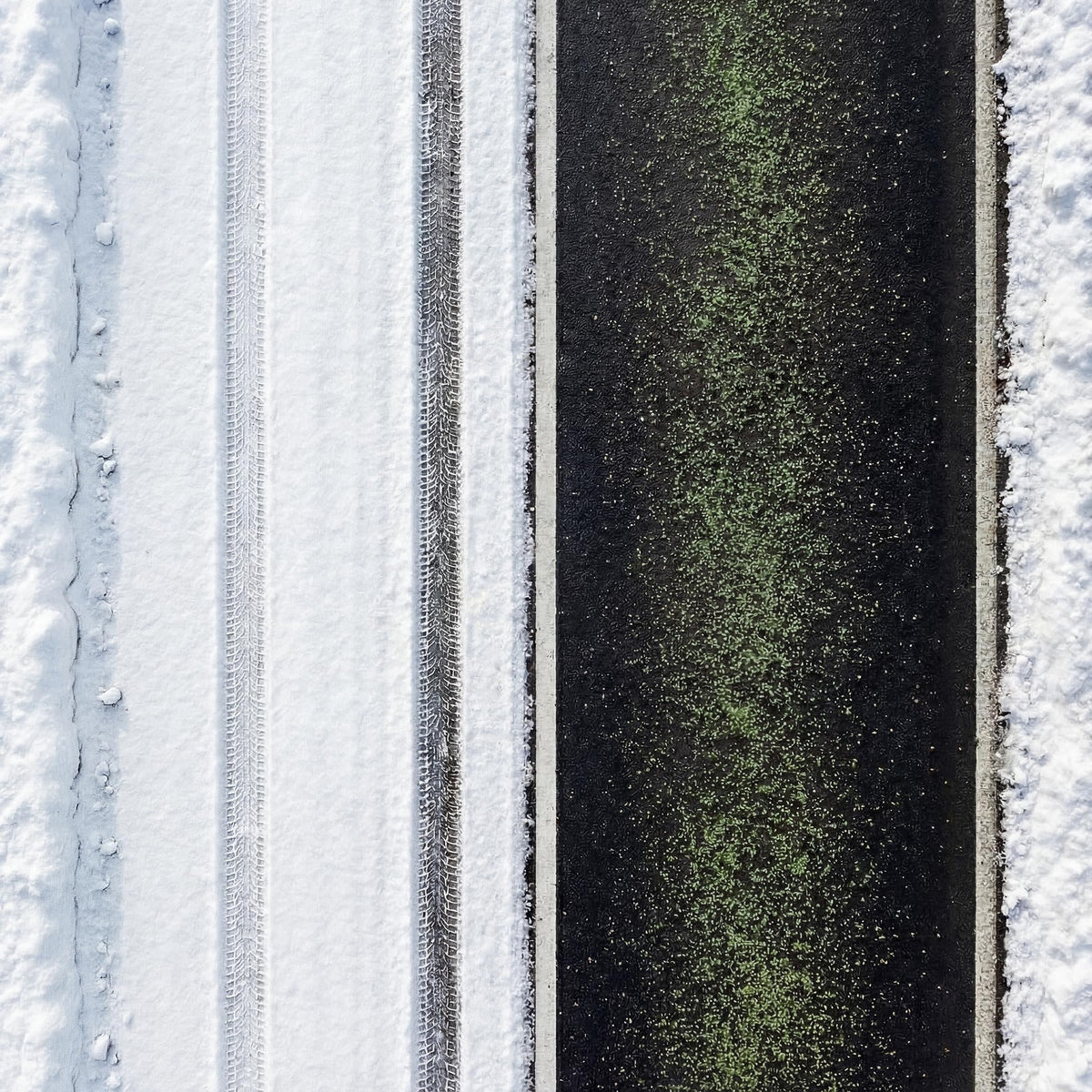 Overhead view of green ice melt granules spread down a dark driveway between snow.